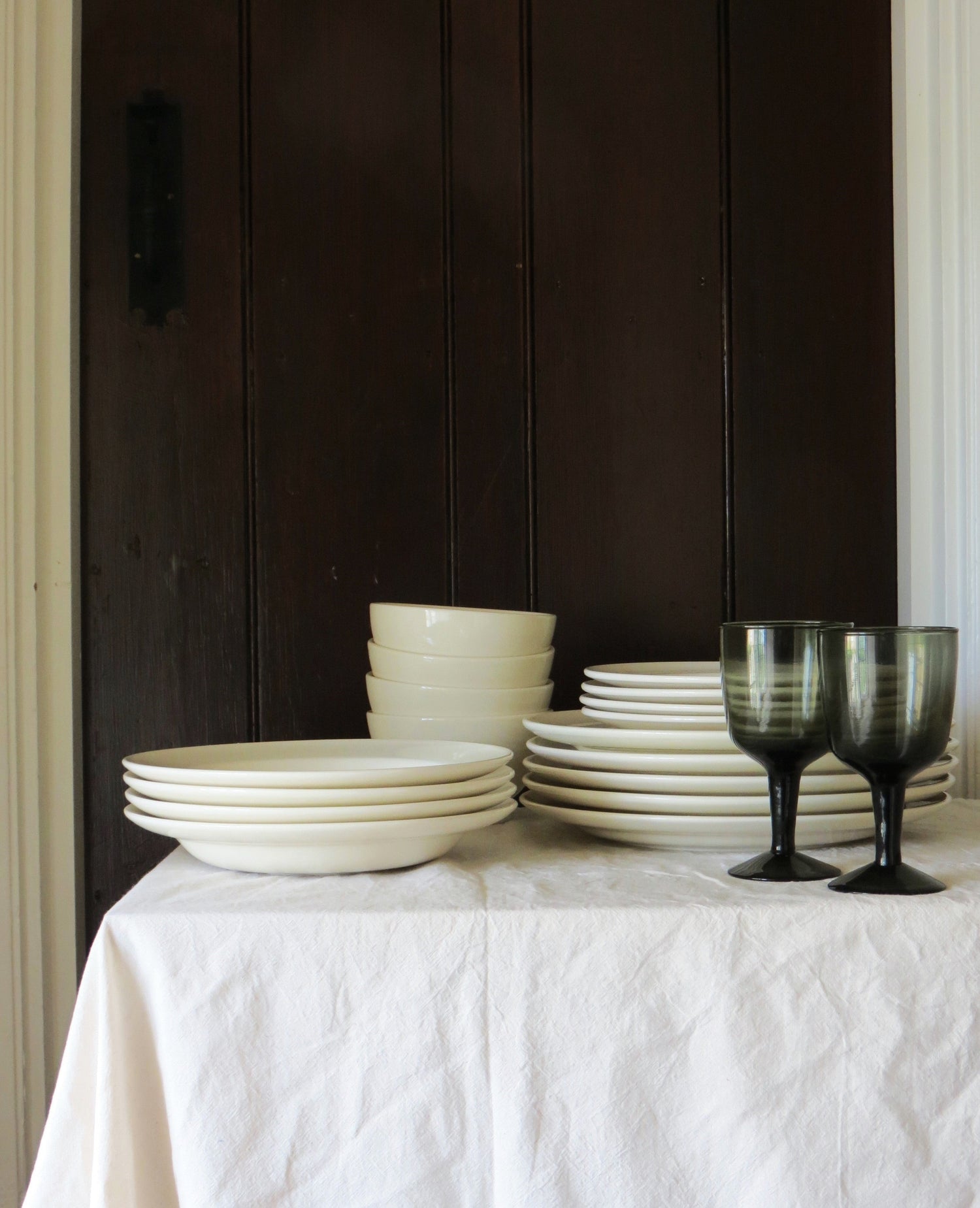 Host tableware collection on white table linen against a dark wood background. 