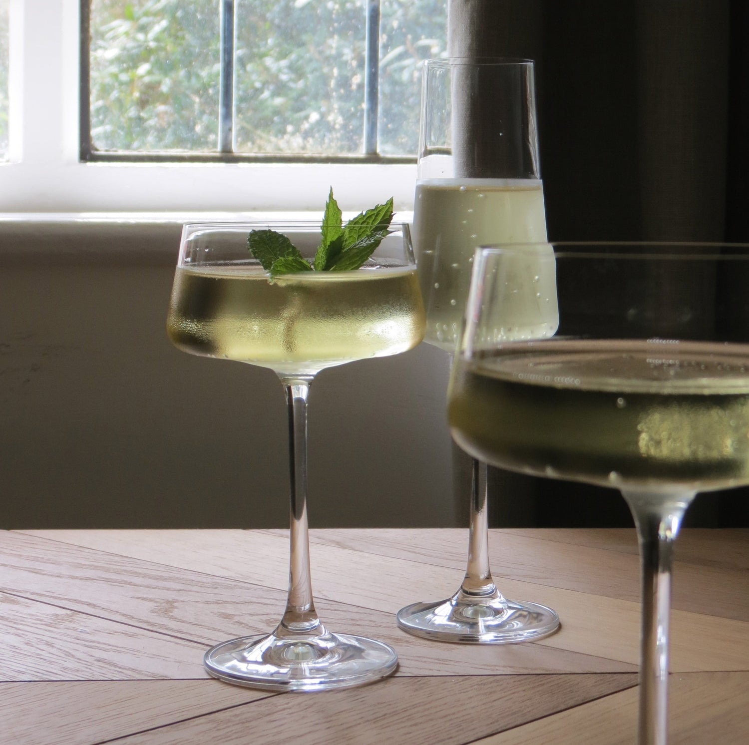 In a cottage setting by the window are glasses, champagne and cocktail glasses with a mint garnish. 