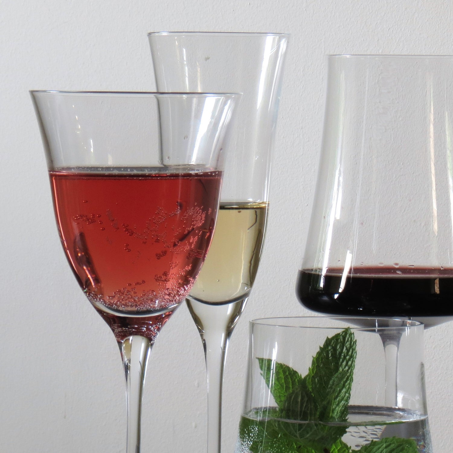 Different glasses with different drinks. 2 wineglasses, 1 Champagne glass and a tumbler.