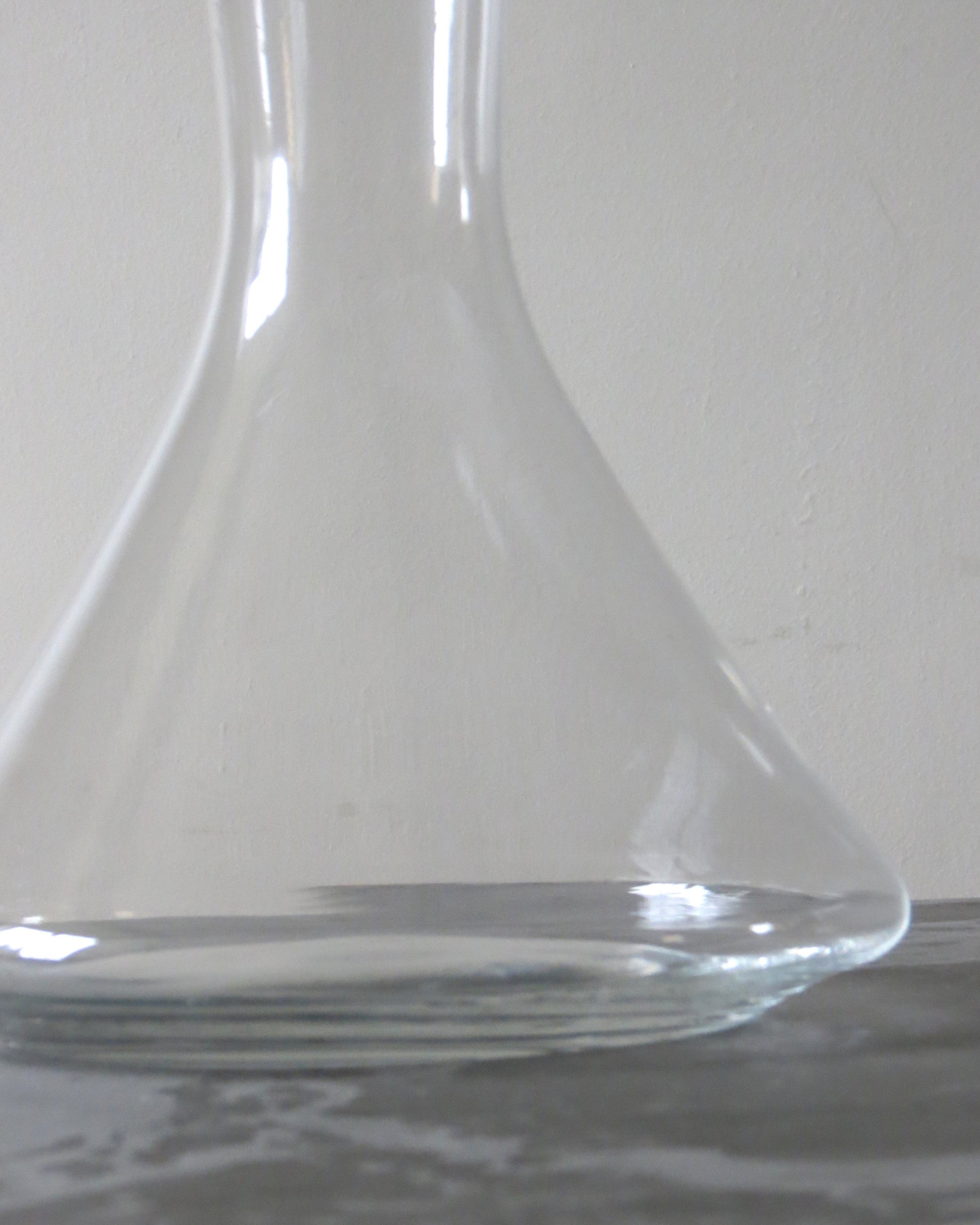 Clear glass carafe on a reflective surface with a light grey background
