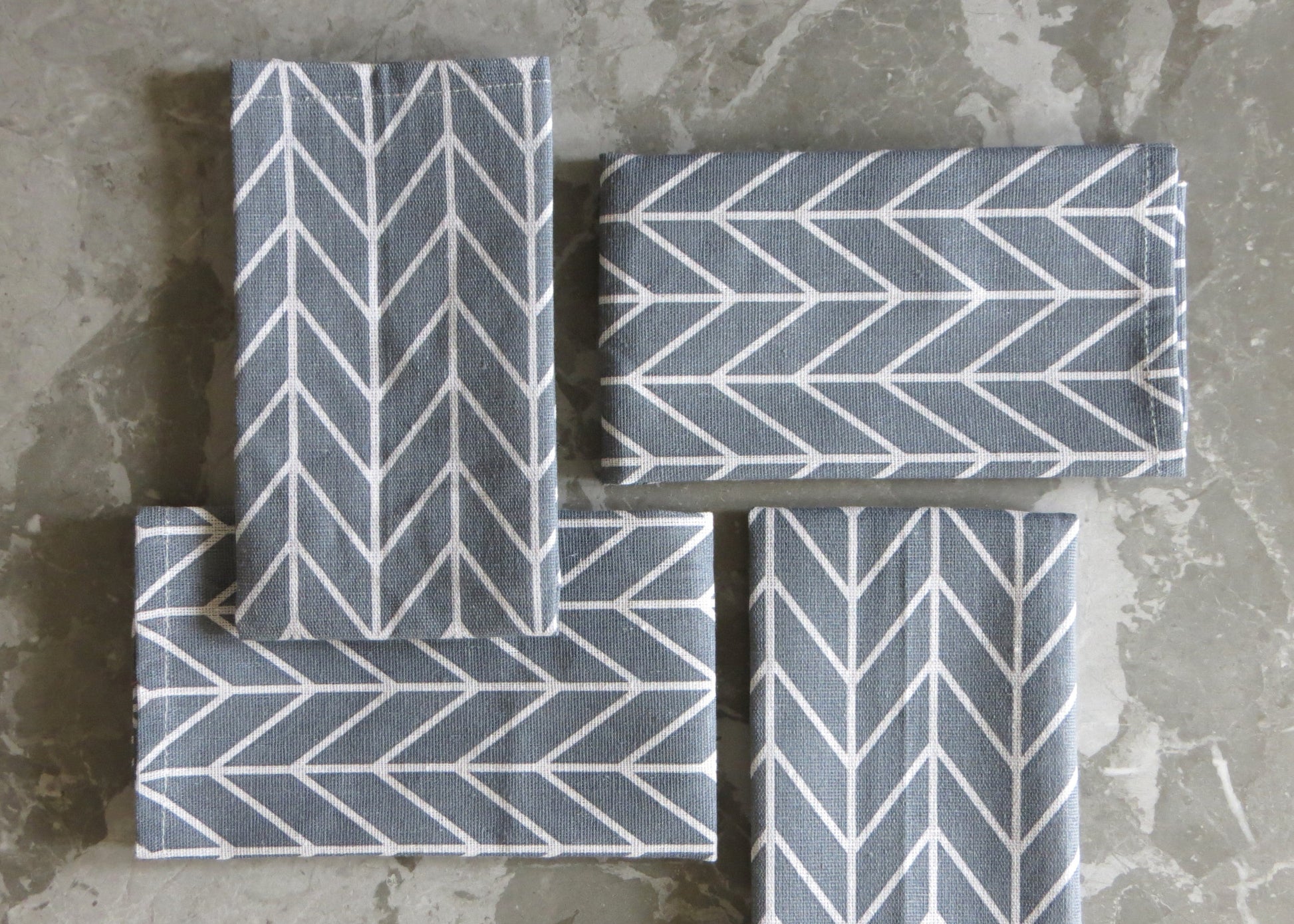 A set of four folded grey napkins with a white chevron pattern, displayed on a grey surface.
