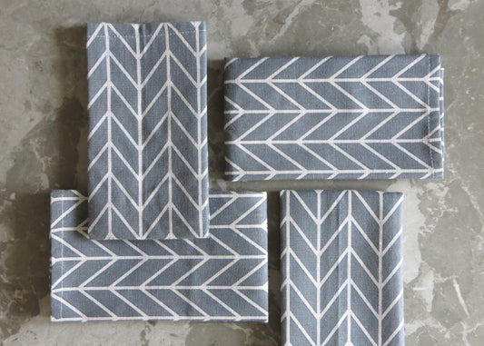 A set of four folded grey napkins with a white chevron pattern, displayed on a grey surface.