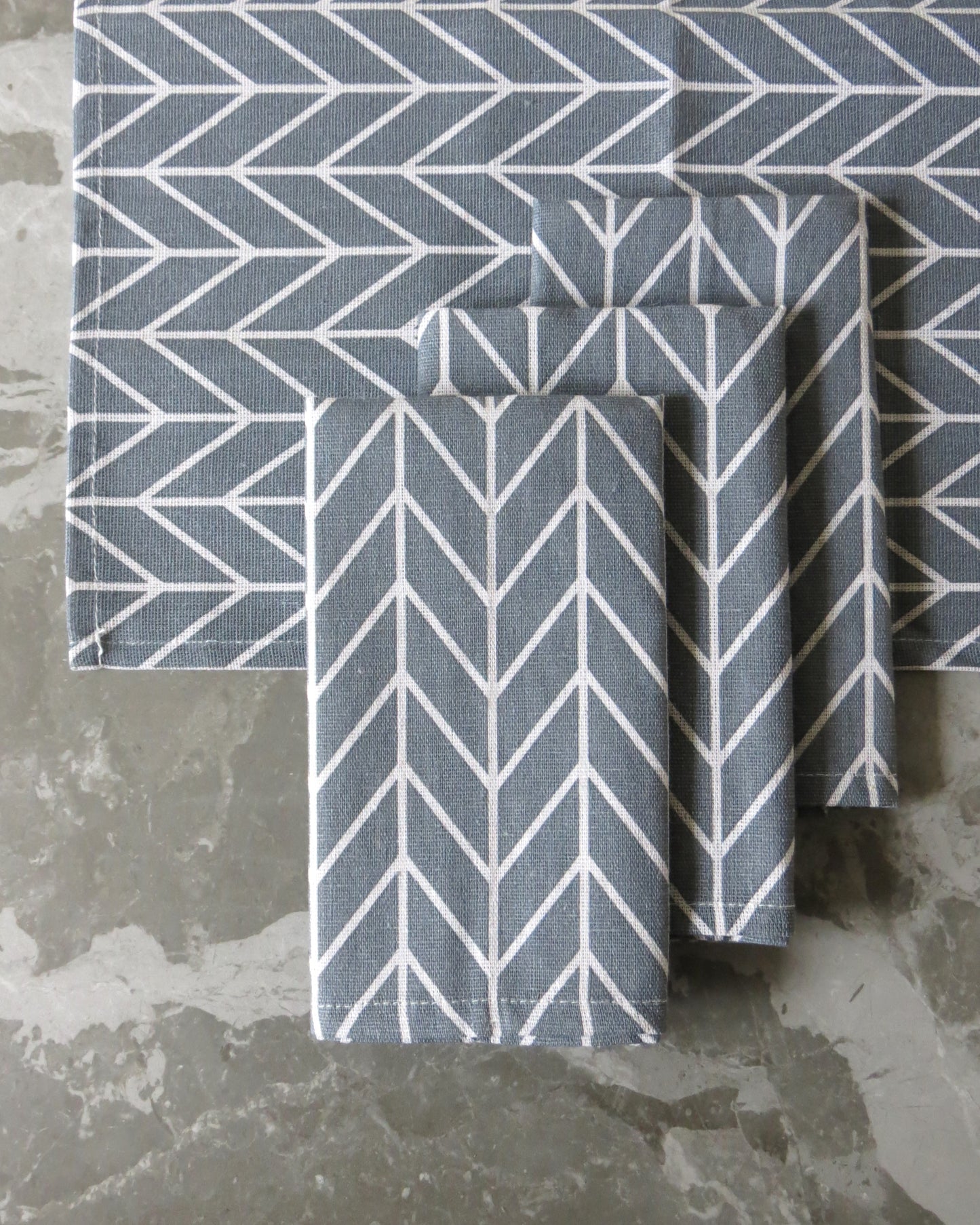A set of four grey chevron pattern cloth napkins folded and placed on a grey surface.