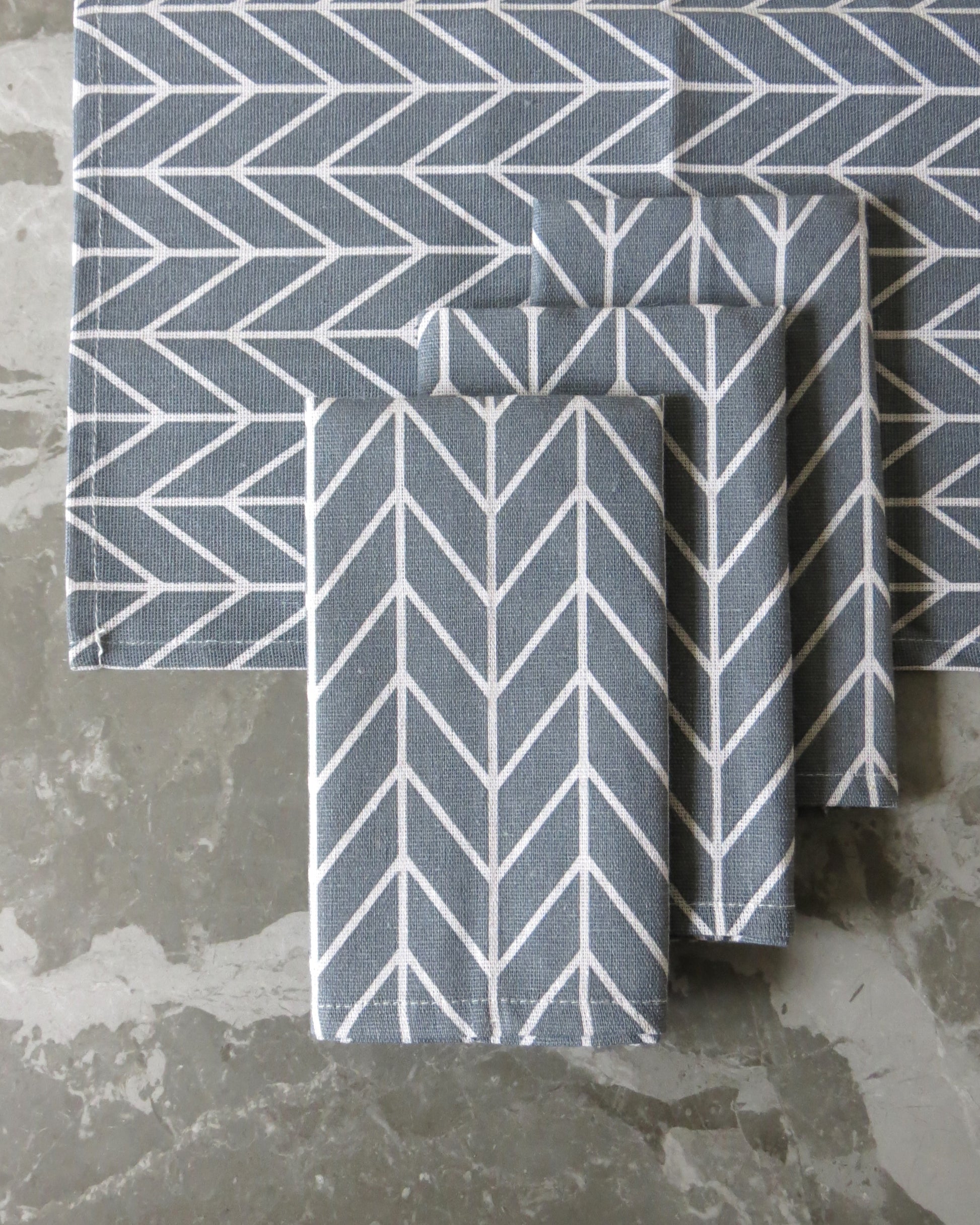 A set of four grey chevron pattern cloth napkins folded and placed on a grey surface.