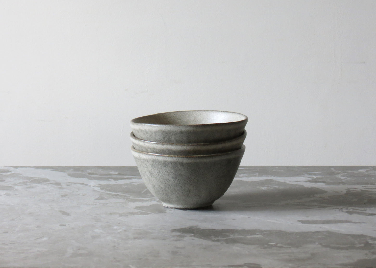 Stack of grey ceramic bowls on a marble surface with a light grey background