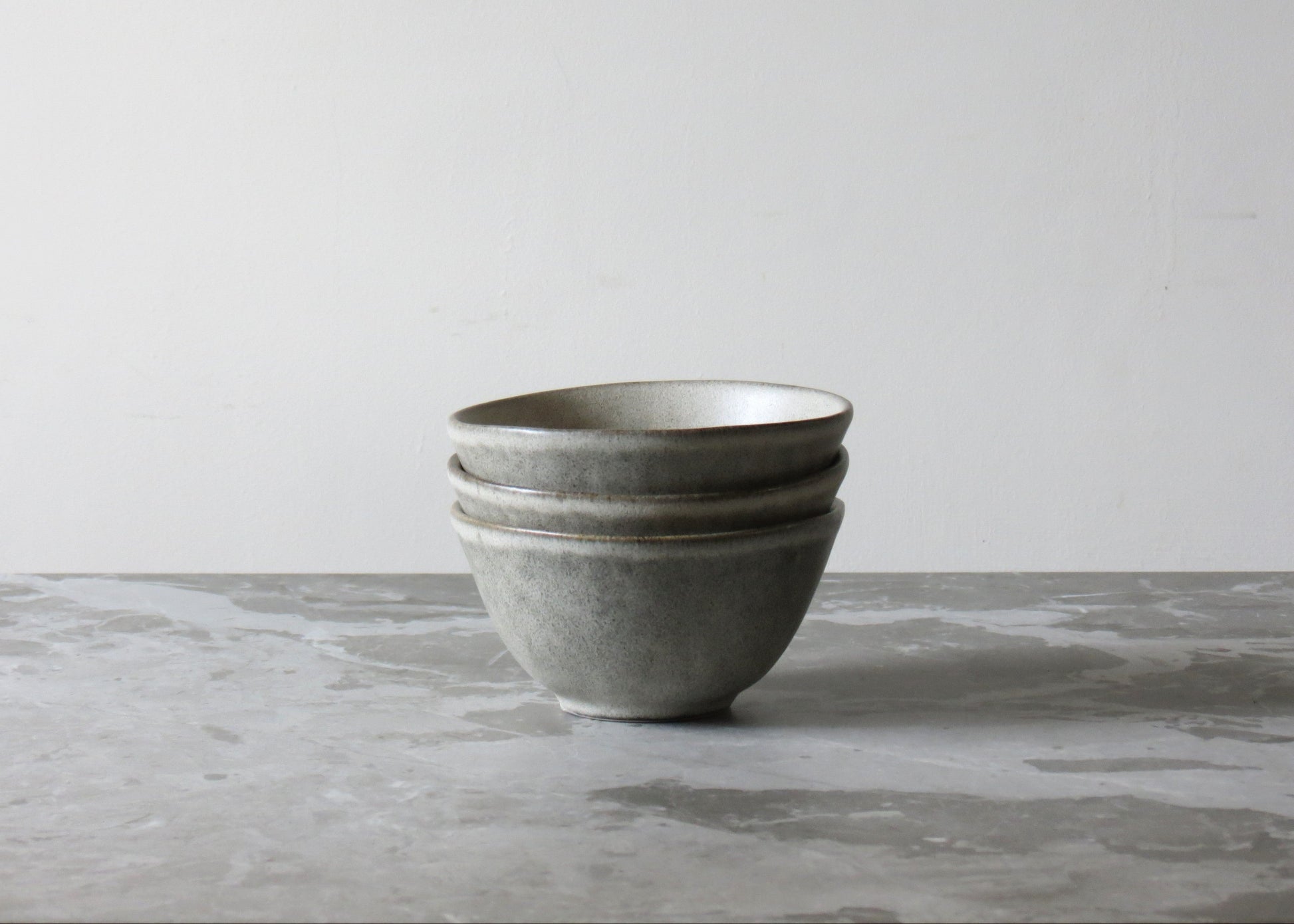 Stack of grey ceramic bowls on a marble surface with a light grey background