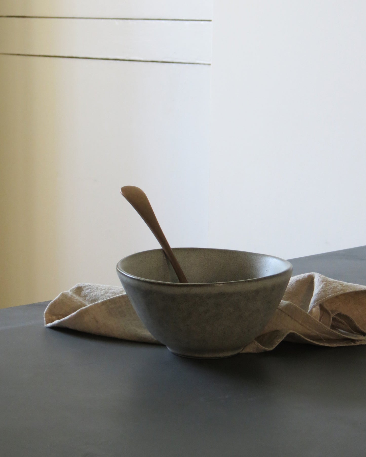 Grey bowl with a spoon on a dark surface with a light background