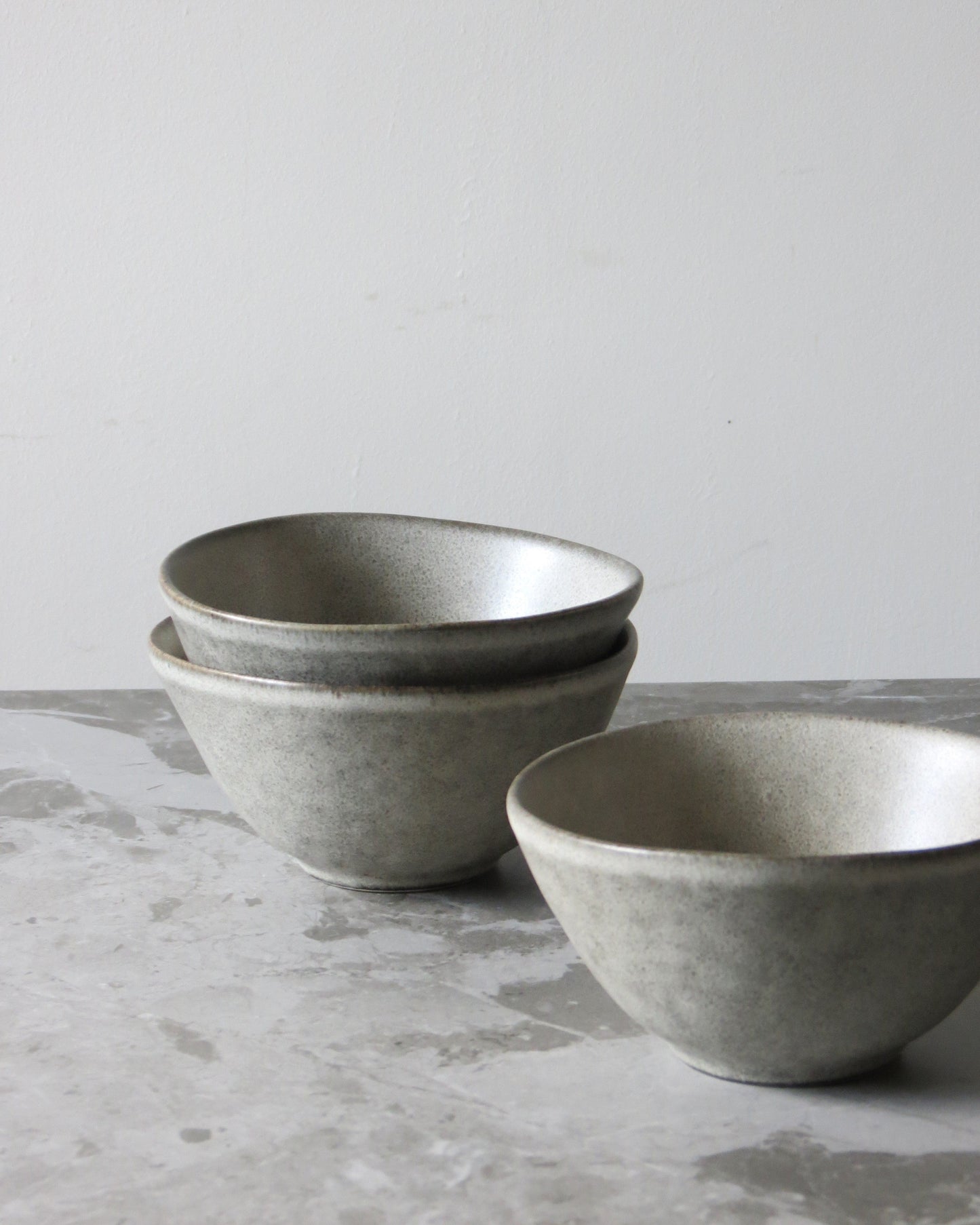 Three grey ceramic bowls on a textured surface with a light grey background