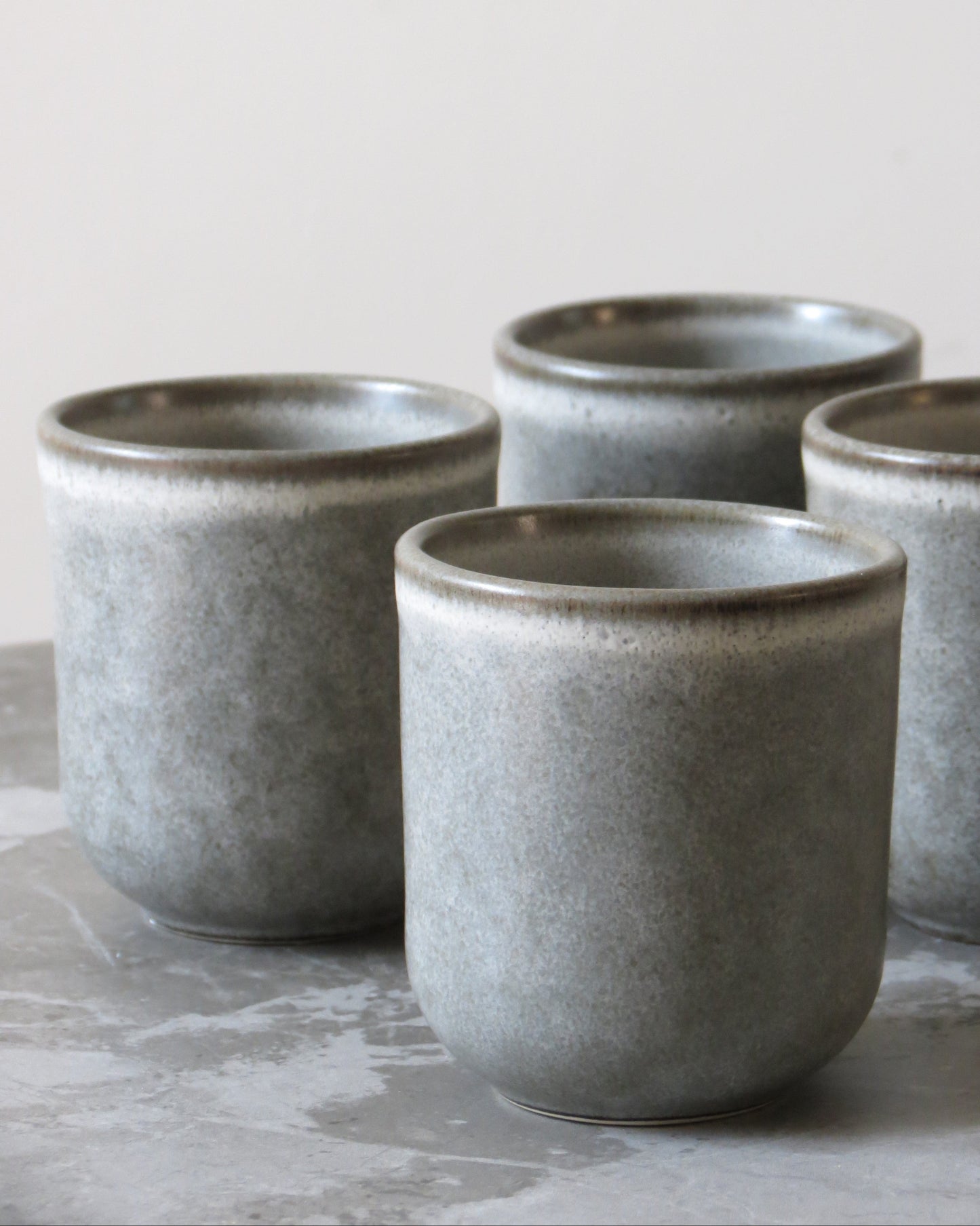 Set of four grey ceramic cups on a light stone surface with a neutral background