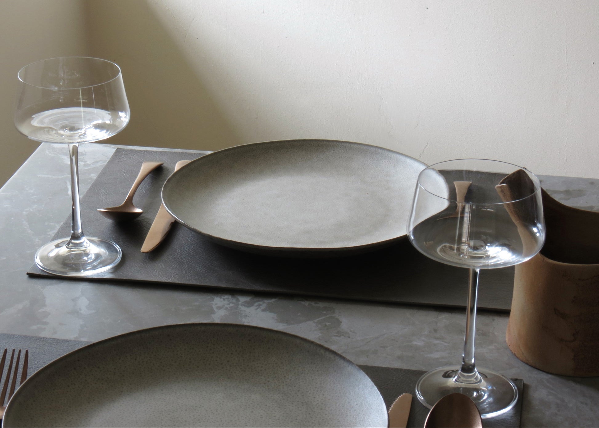 Dining table setting with gray plates, wine glasses, and cutlery on a neutral background