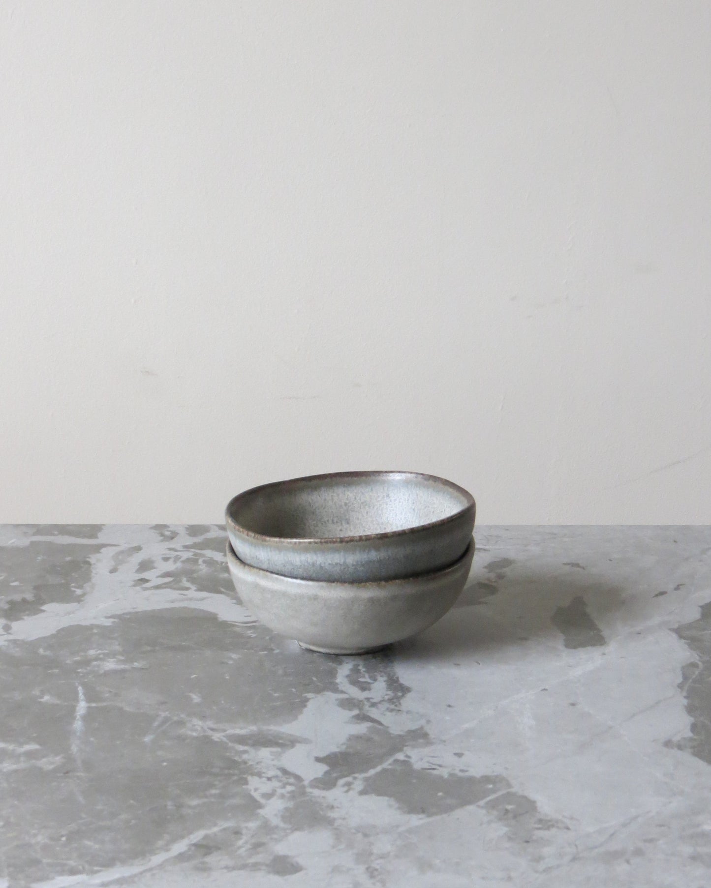Two grey ceramic bowls stacked on a marble surface with a light grey background