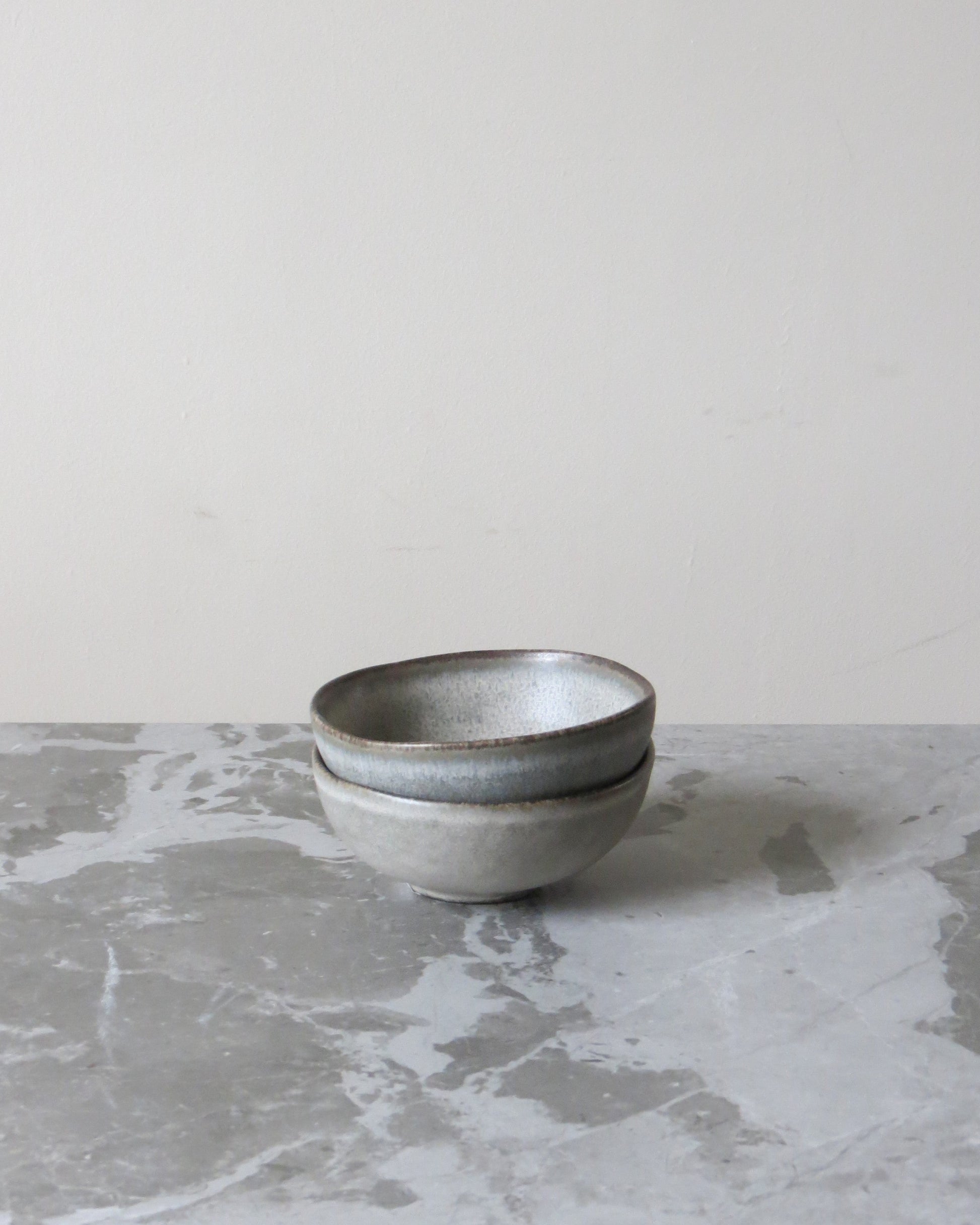 Two grey ceramic bowls stacked on a marble surface with a light grey background