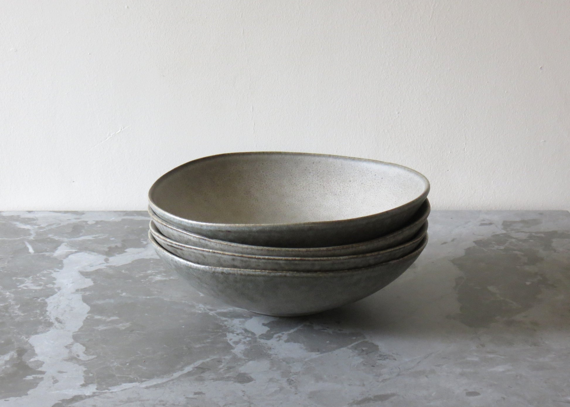 A stack of grey ceramic pasta bowls with a matte finish on a marble surface.