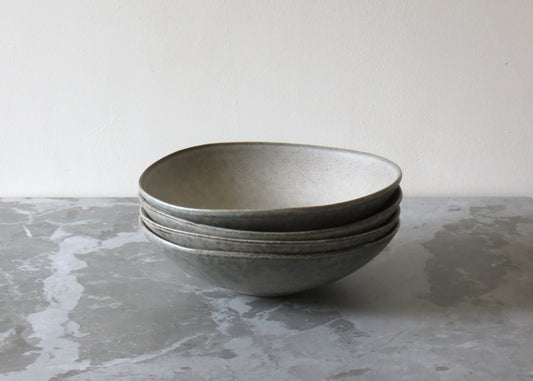 A stack of grey ceramic pasta bowls with a matte finish on a marble surface.