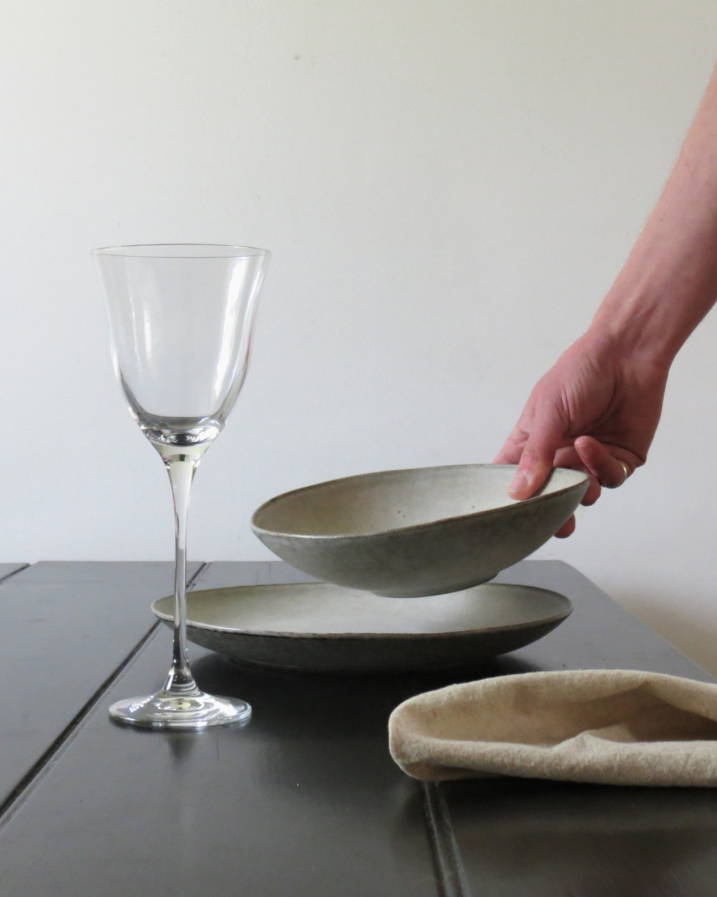 Hand holding a ceramic bowl next to a wine glass on a wooden table.