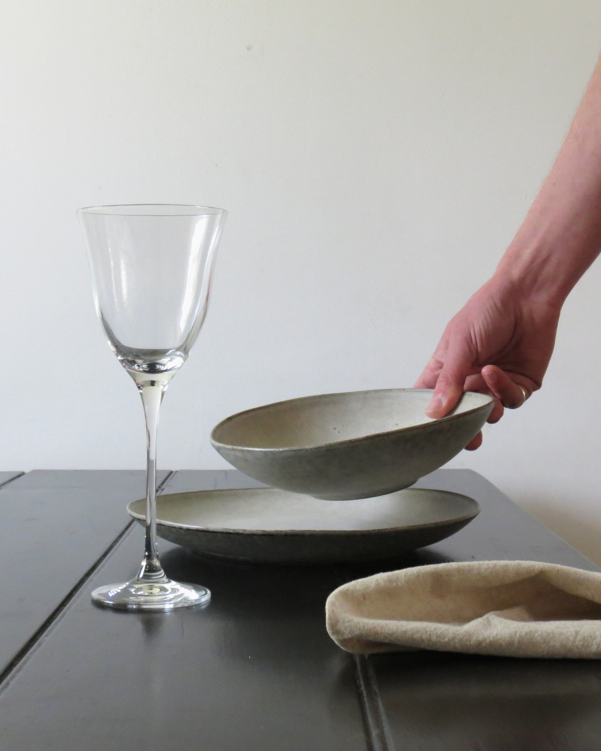 Hand holding a ceramic bowl next to a wine glass on a wooden table.