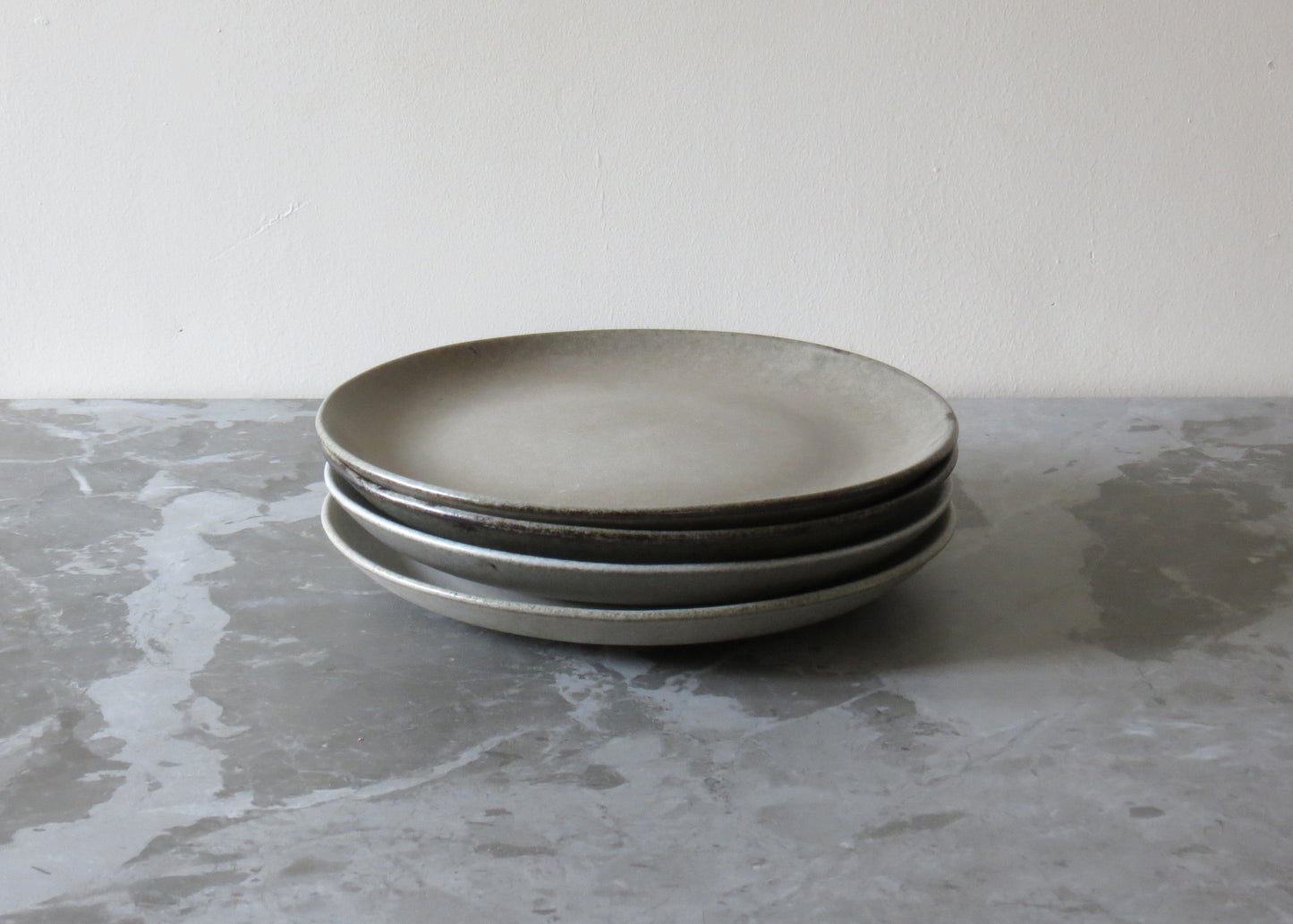 A stack of beige clay side plates with a matte finish on a grey marble surface.