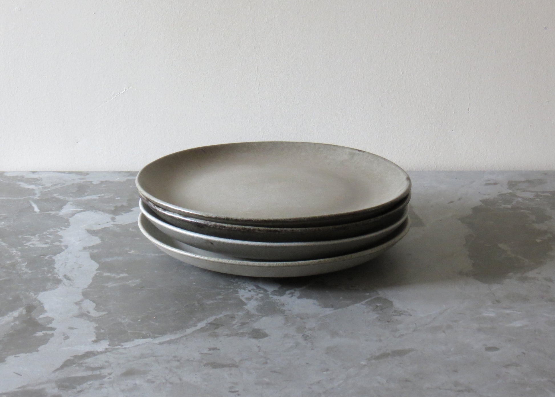 A stack of beige clay side plates with a matte finish on a grey marble surface.