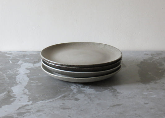 A stack of beige clay side plates with a matte finish on a grey marble surface.