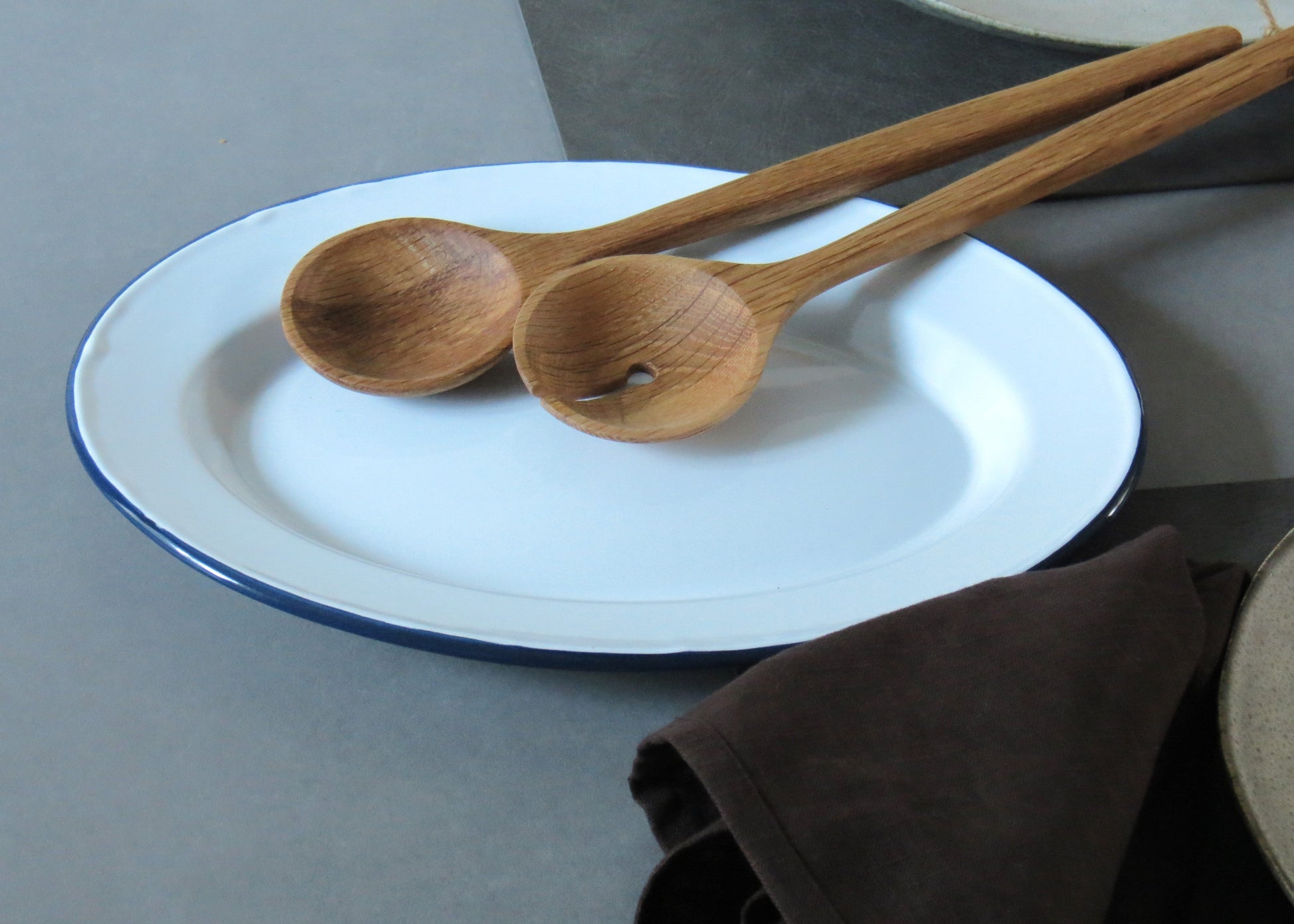 Two wooden spoons on a white plate with a brown napkin in the background.