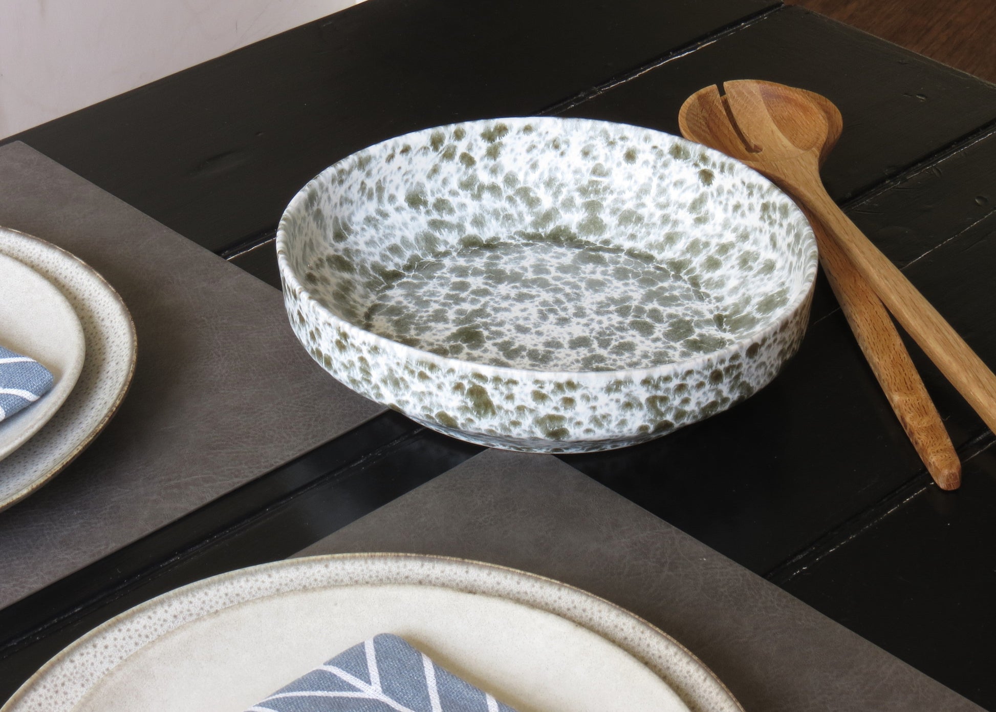 Speckled ceramic bowl on a dark wooden table with wooden spoons.