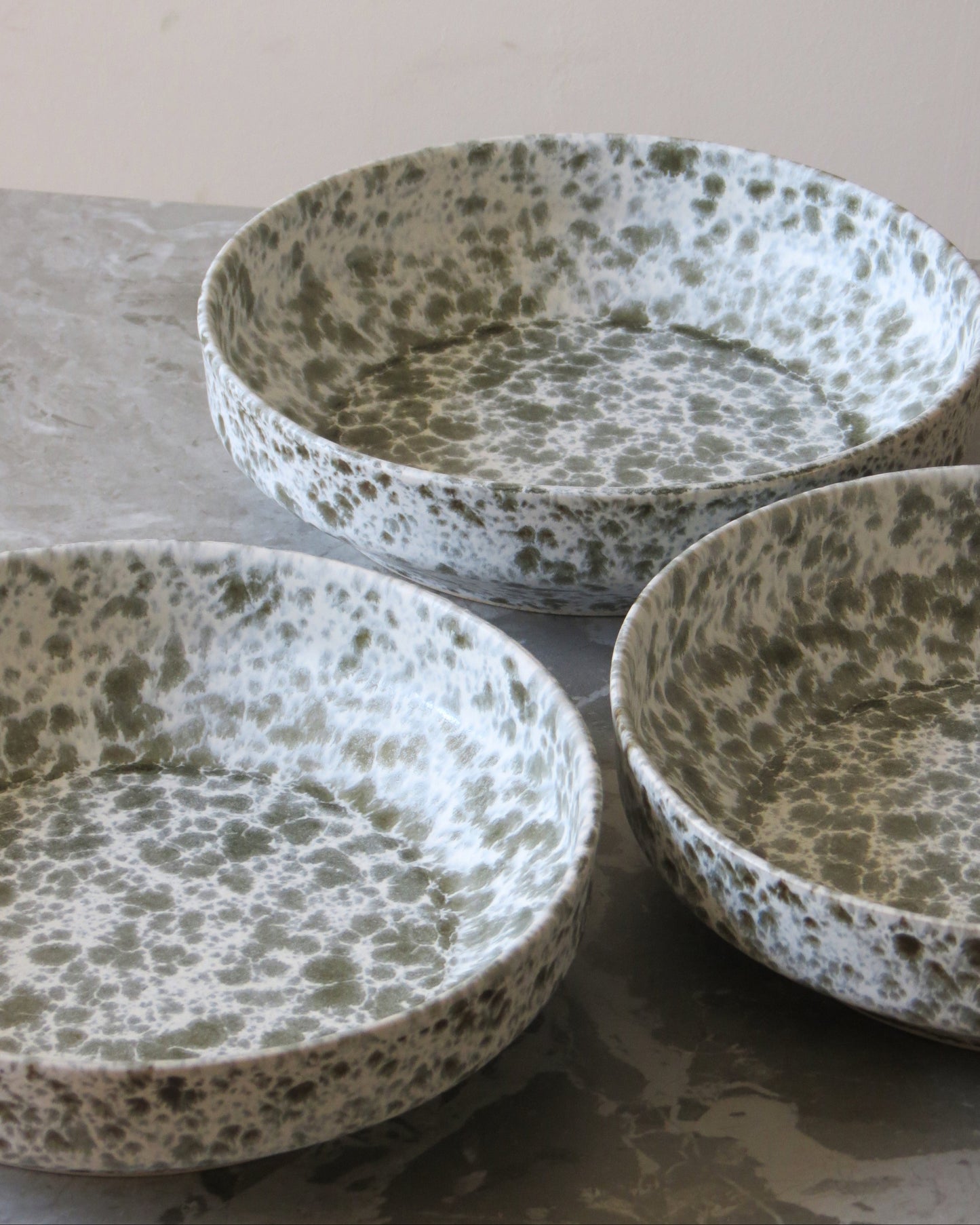Three ceramic bowls with speckled pattern on a textured surface