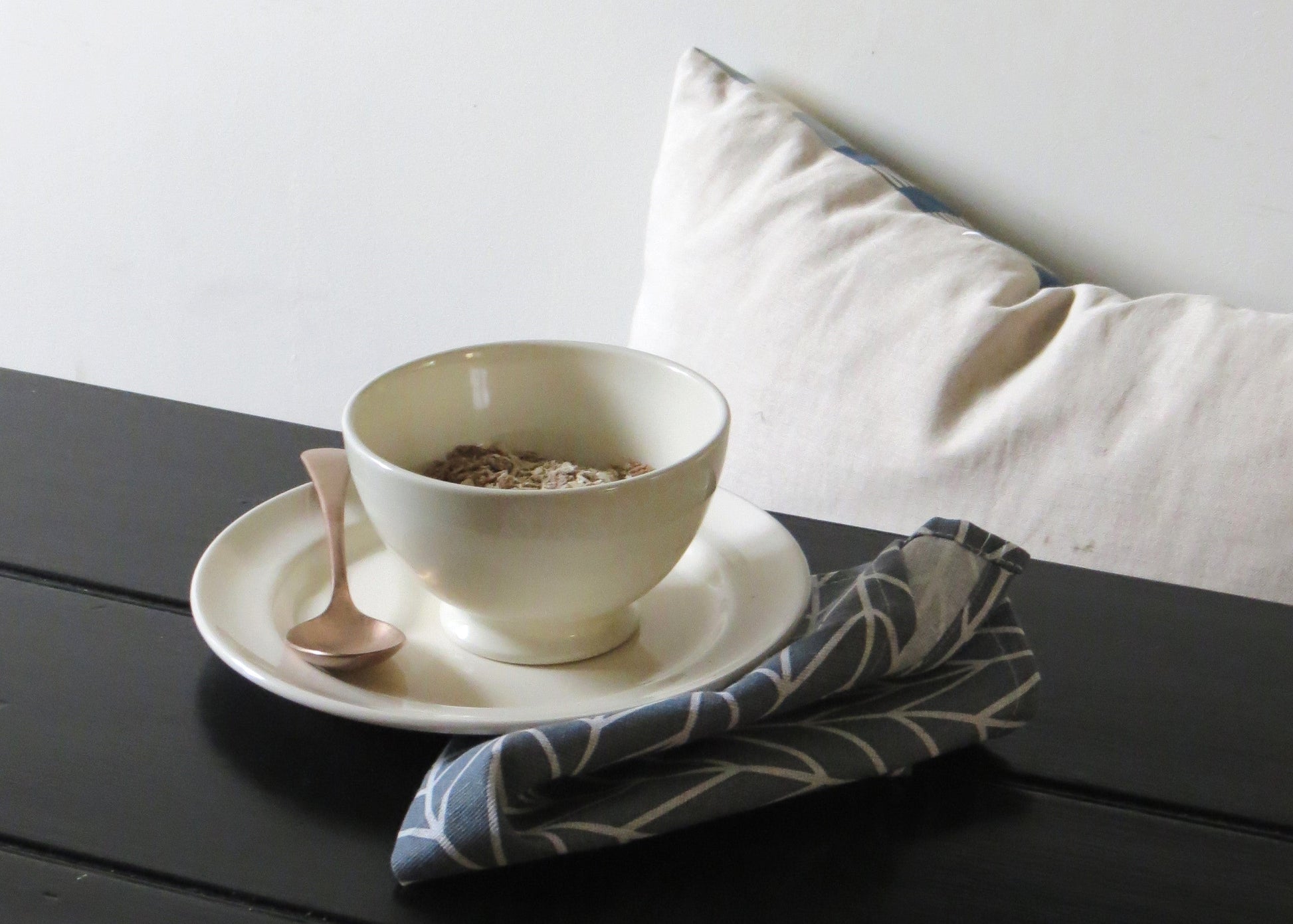 Ceramic cereal bowl on a black wooden surface with a white pillow in the background