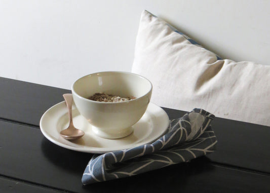 Ceramic cereal bowl on a black wooden surface with a white pillow in the background