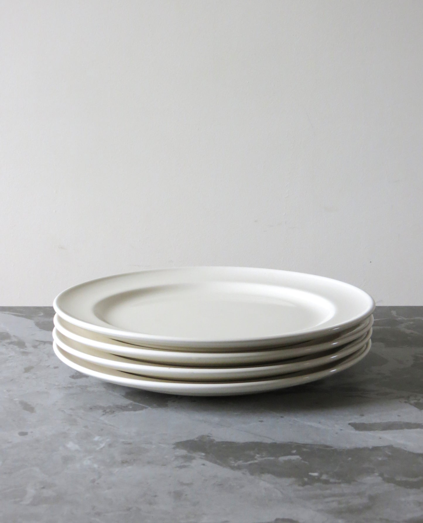 Stack of white plates on a grey surface with a white background.