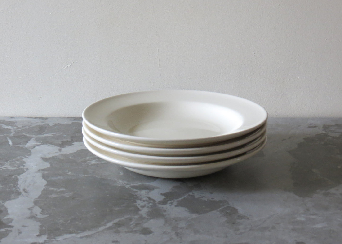 A stack of cream ceramic pasta bowls on a grey marble surface.