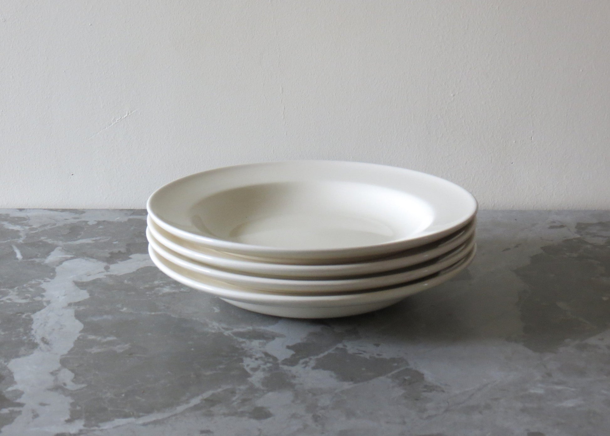 A stack of cream ceramic pasta bowls on a grey marble surface.