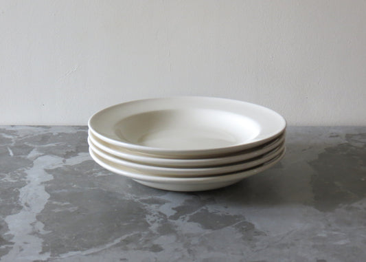 A stack of cream ceramic pasta bowls on a grey marble surface.