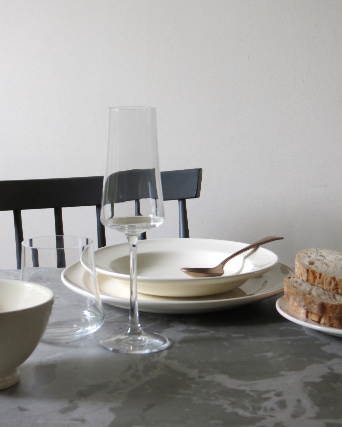Dining table setting with plates, glasses, and bread on a grey stone surface.