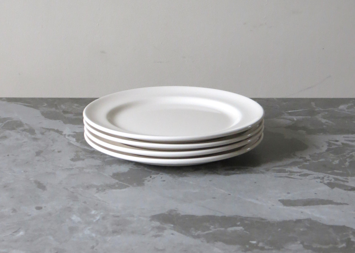 Stack of white plates on a grey surface with a plain background.
