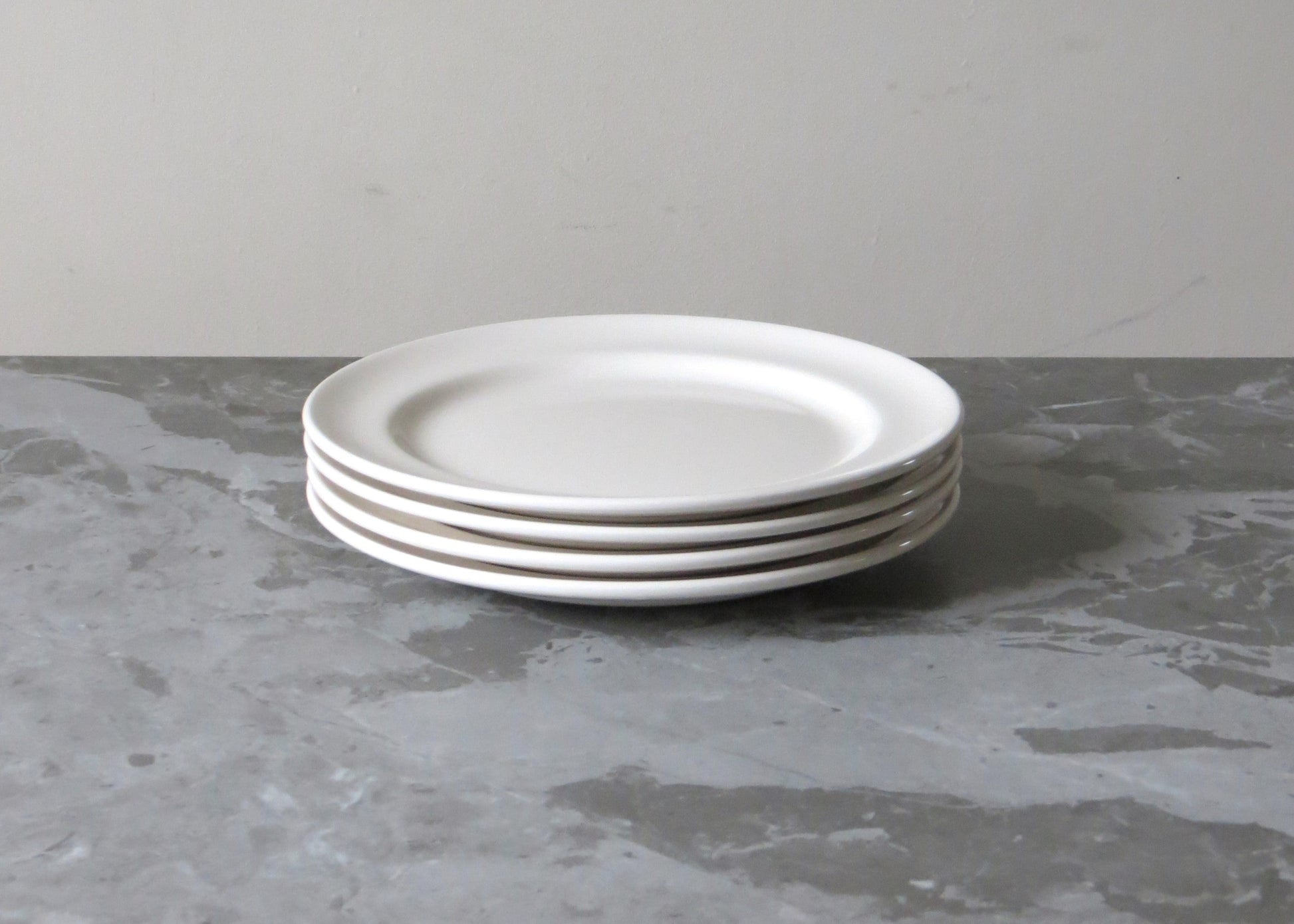 Stack of white plates on a grey surface with a plain background.