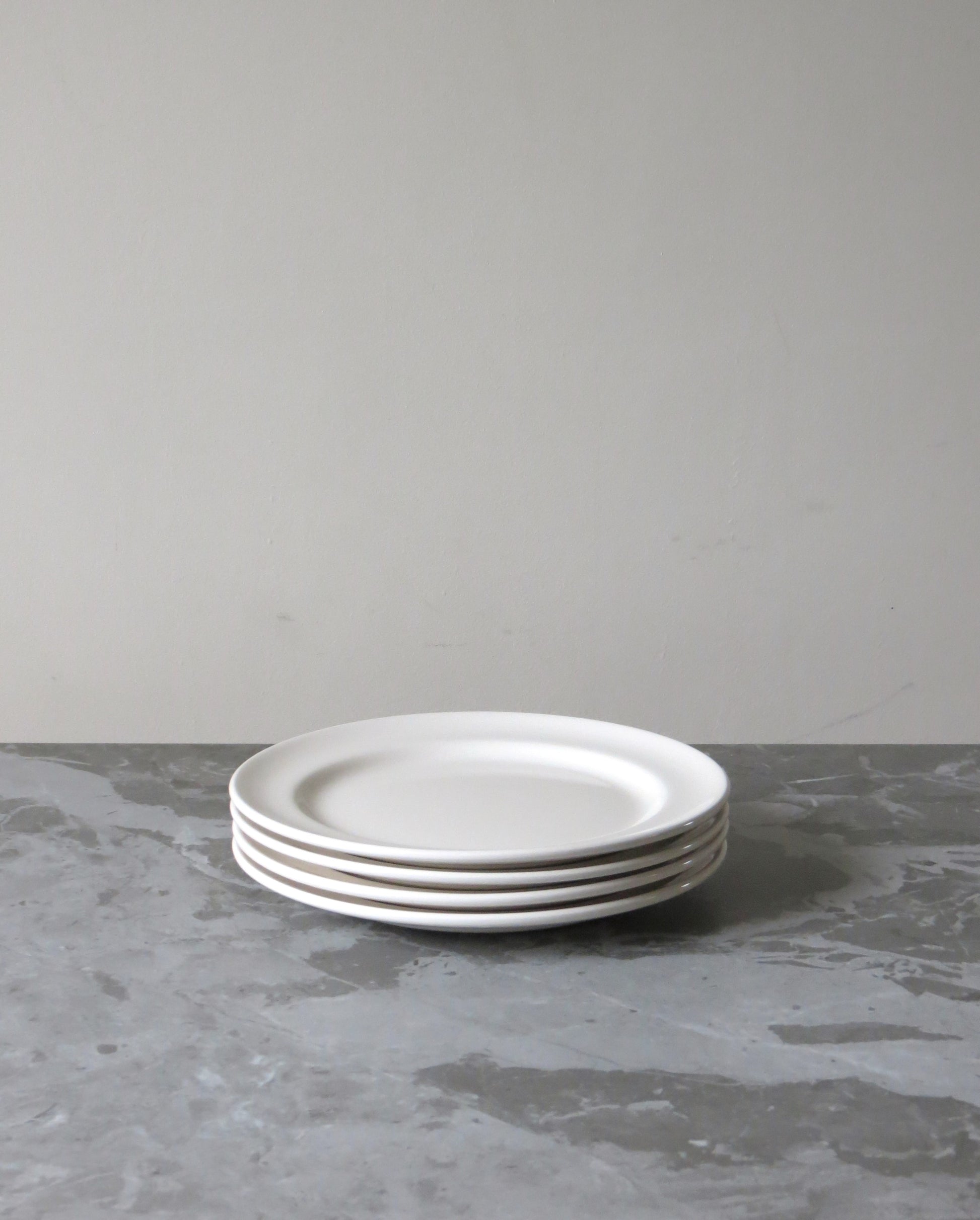 Stack of white ceramic plates on a grey surface with a neutral background
