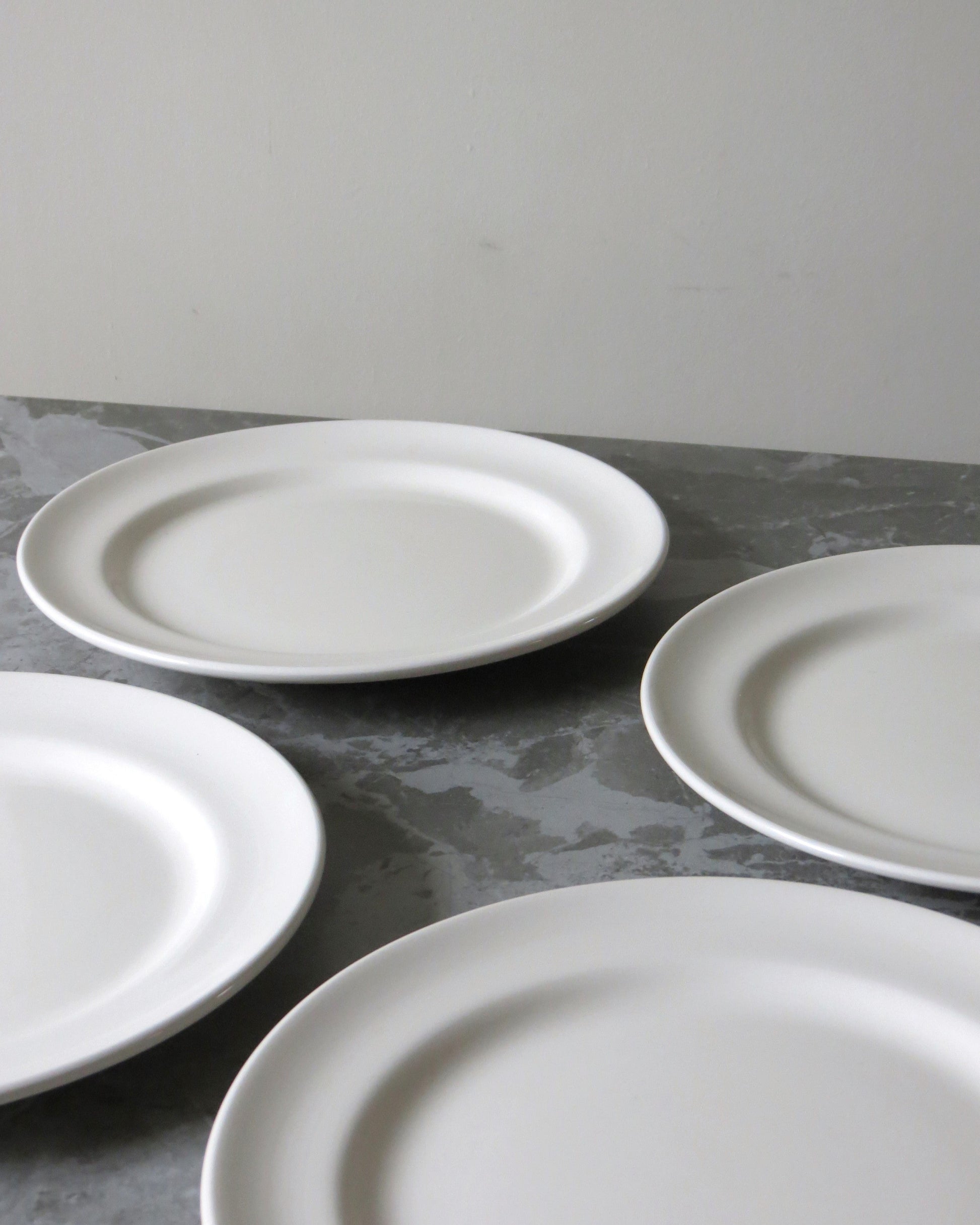 Four white ceramic plates on a grey surface with a plain background