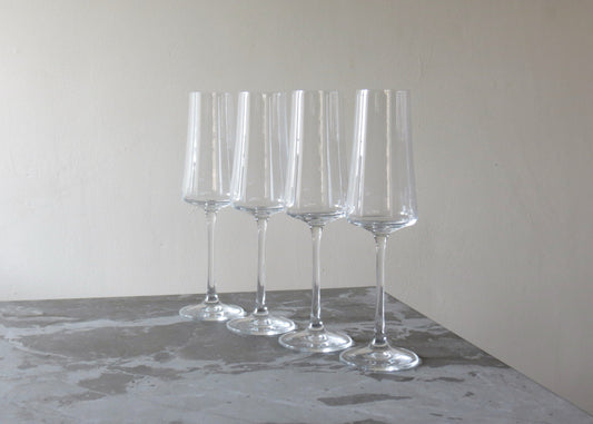 Set of four clear Champagne glasses on a grey surface with a neutral background