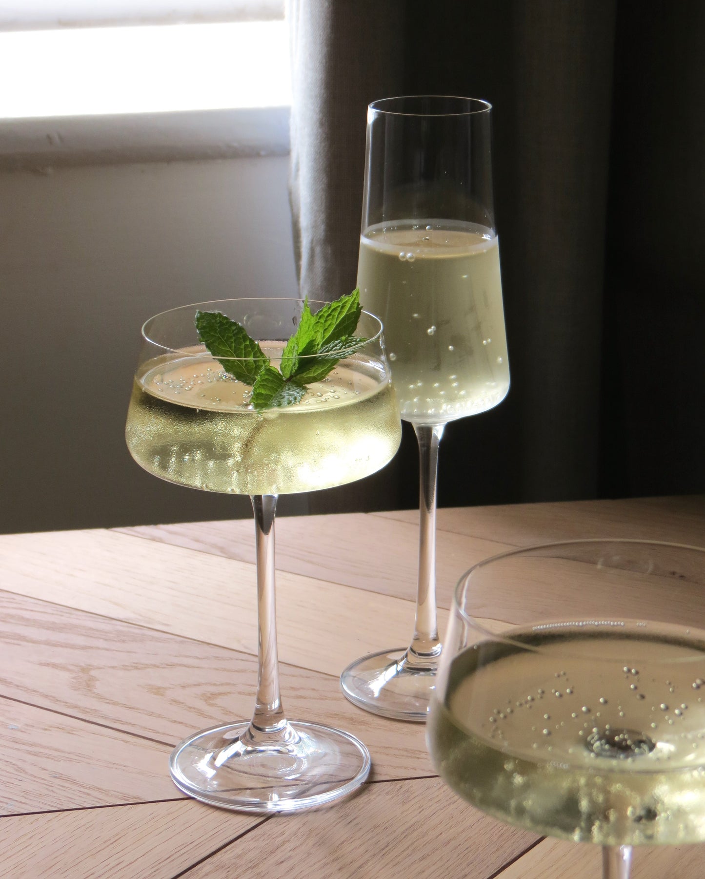 Two glasses of champagne with mint leaves on a wooden table.