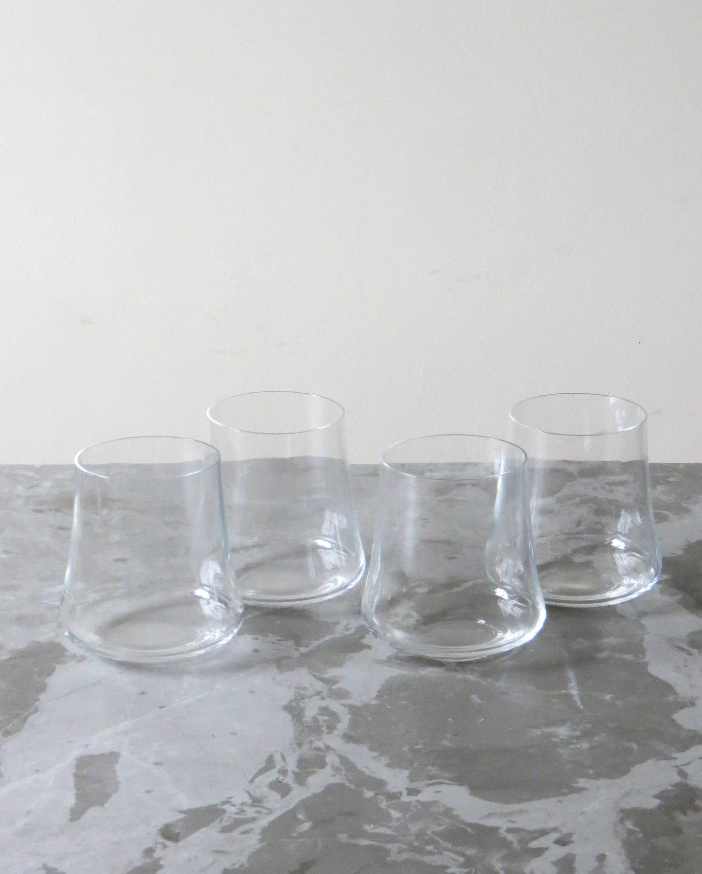 Four clear glass tumblers on a grey marble surface with a white background.