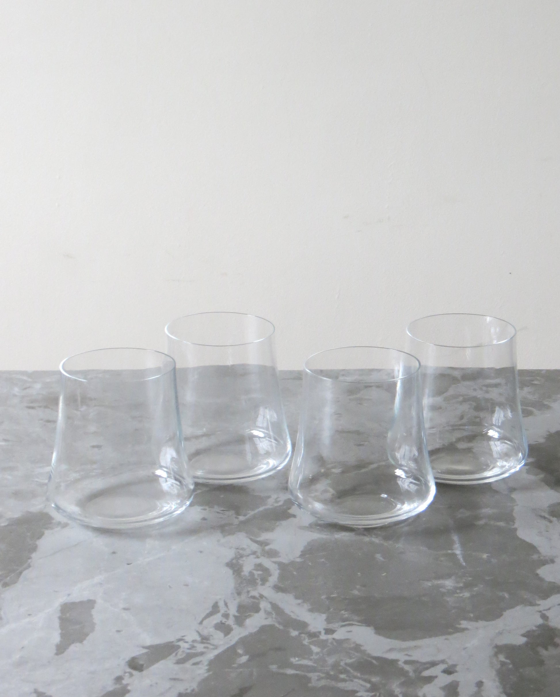 Four clear glass tumblers on a grey marble surface with a white background.