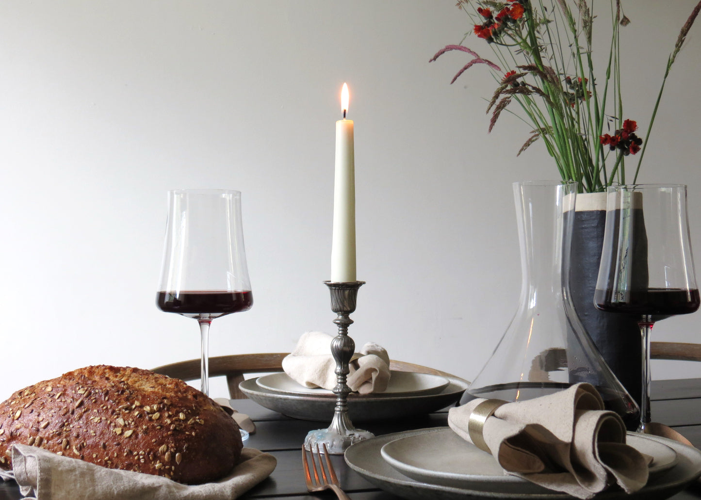 A set of wine glasses on a table with a lit candle, a piece of bread, and a floral arrangement, filled with red wine.