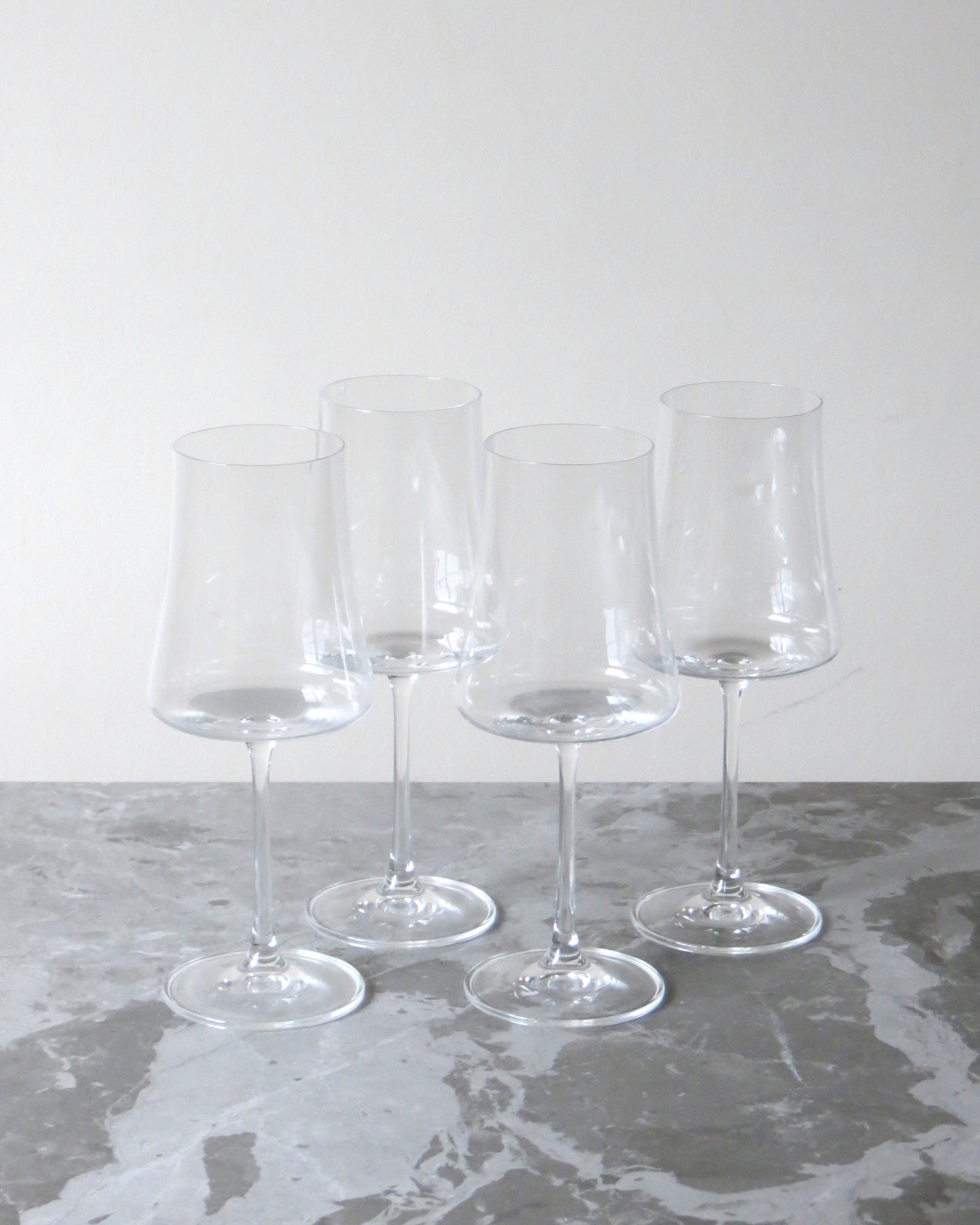 Set of four clear wine glasses on a grey surface with a white background