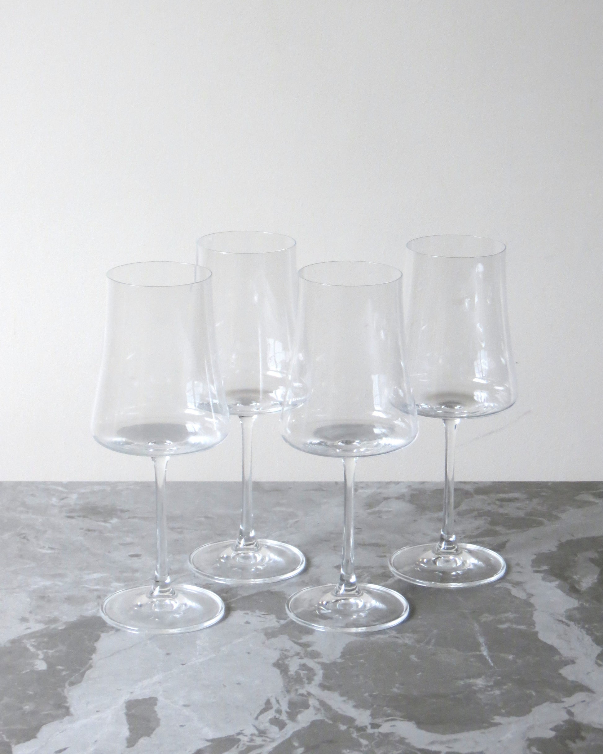 Set of four clear wine glasses on a grey surface with a white background