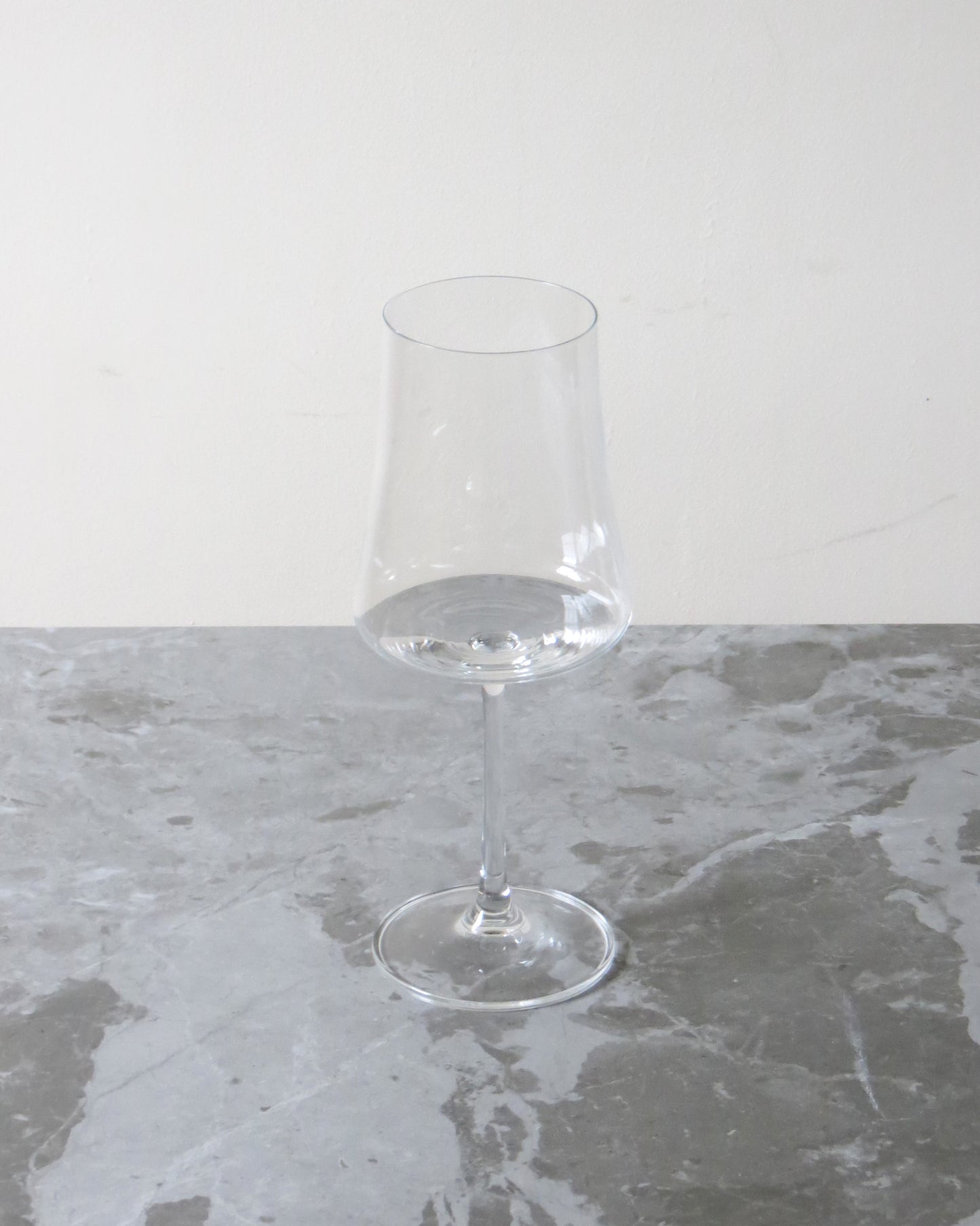 Clear wine glass on a grey marble surface with a white background.