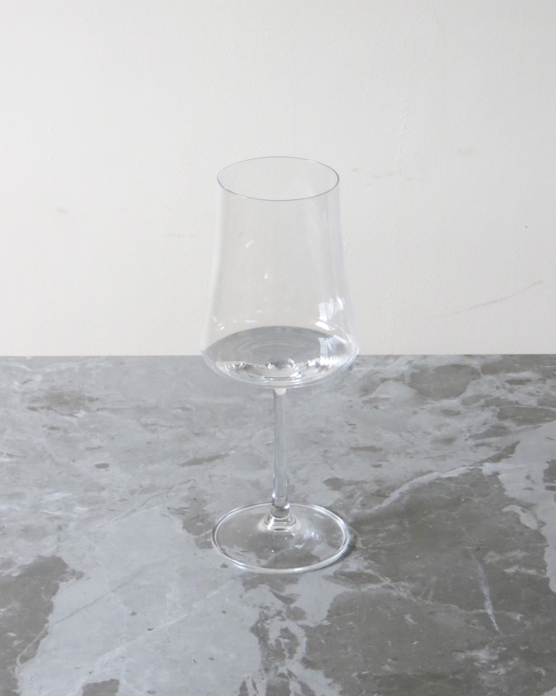 Clear wine glass on a grey marble surface with a white background.