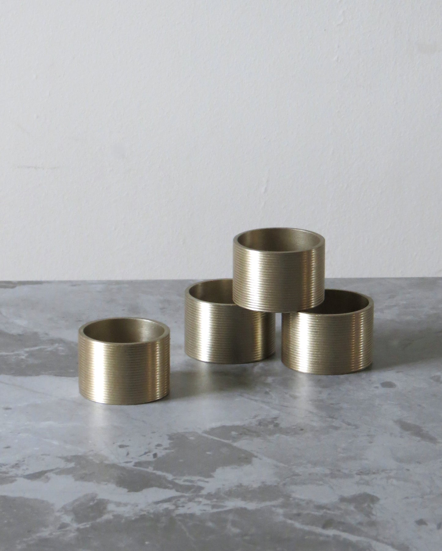 Four brass napkin rings on a grey concrete surface.