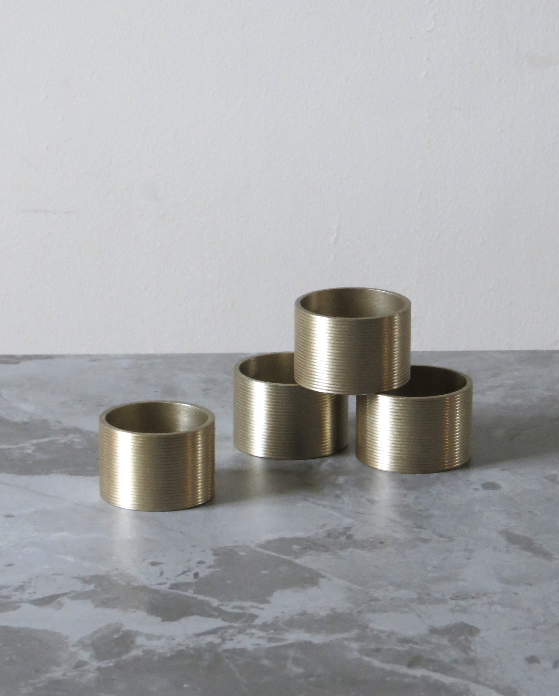 Four brass napkin rings on a grey concrete surface.