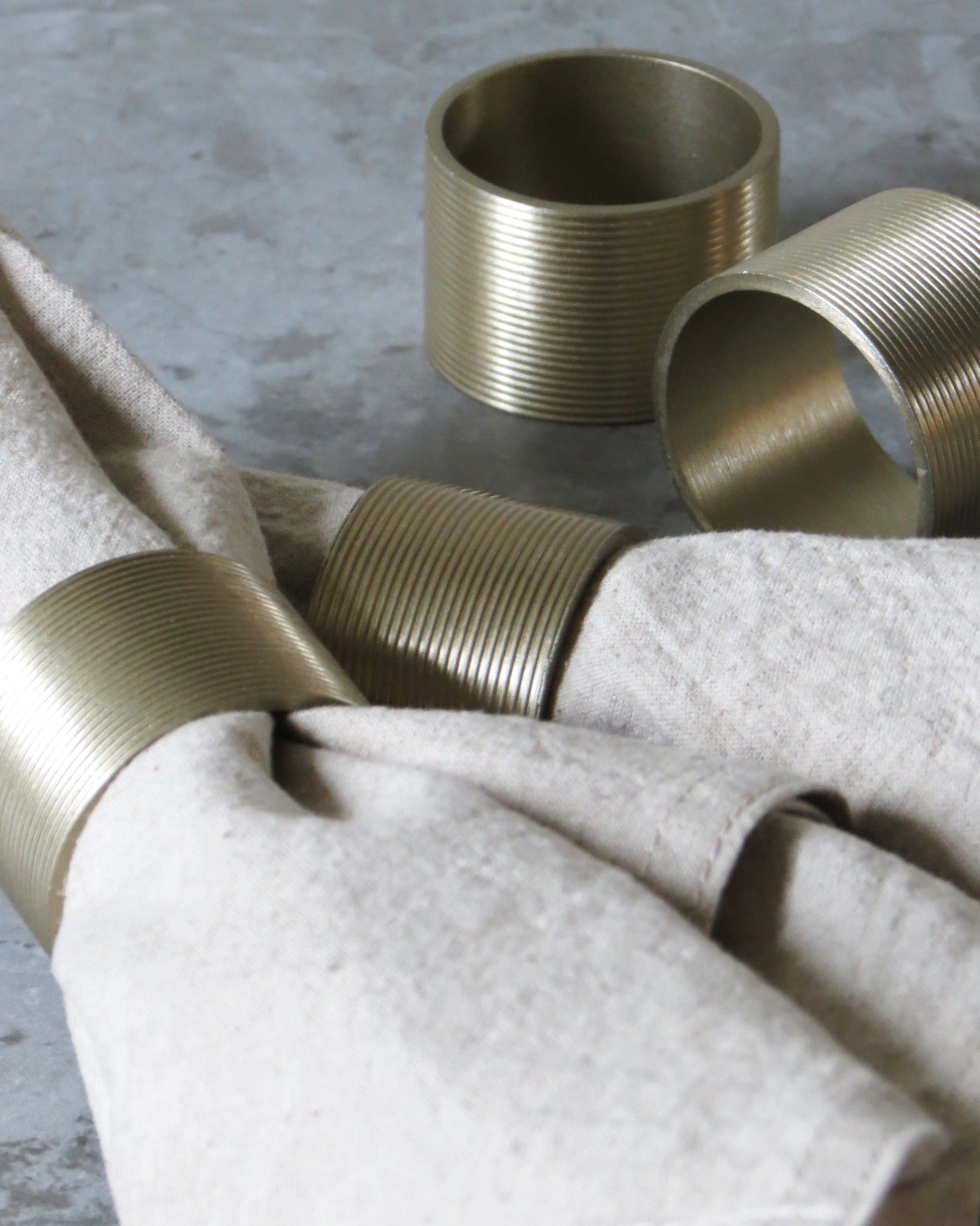 A set of gold-coloured lined napkin rings displayed on a table with a napkin.