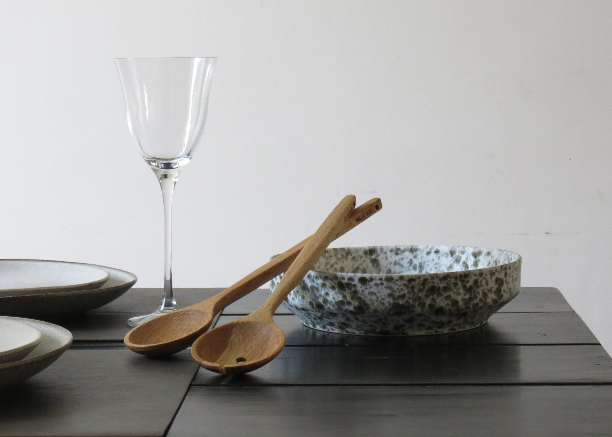 Dinner setting with ceramic bowl, oak wooden spoons, and glass on a wooden table.